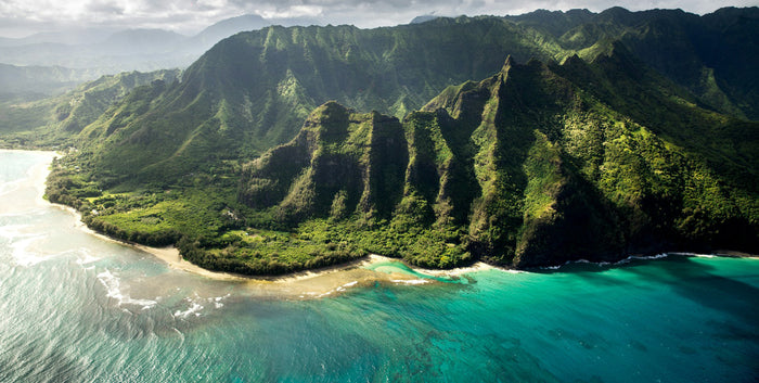 Aerial view of a Hawaiian beach with turquoise water, white sand, palm trees, and volcanic cliffs