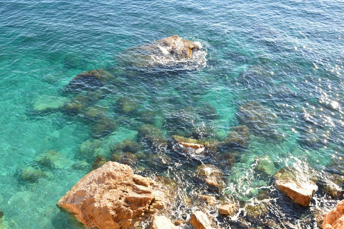 Aerial view of a hidden beach in Croatia with clear turquoise water, rocky coastline, and lush green surroundings